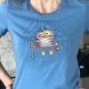 Cross stitch embroidery of a cute yoga cat sitting on a mat with small props and bright colors, displayed on t-shirt