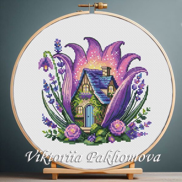 Purple fairy house cross stitch pattern displayed in a wooden embroidery hoop with lavender floral details