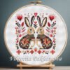 Romantic Bunny cross stitch pattern displayed in a wooden embroidery hoop with warm folk‑art flowers