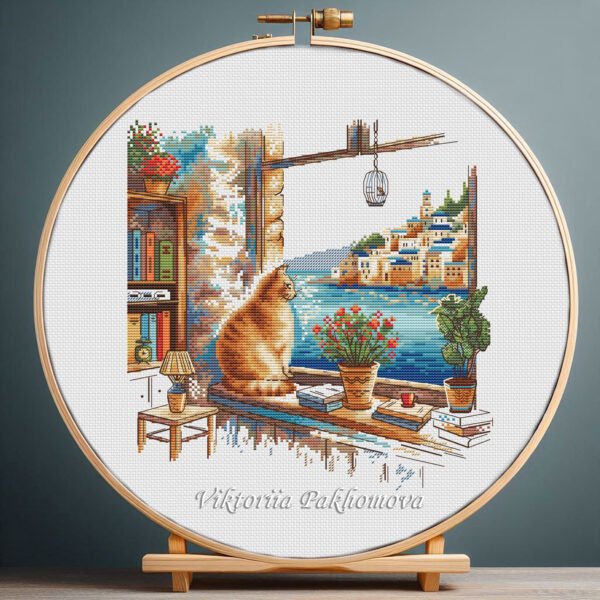131 Cross stitch embroidery of a ginger cat sitting on a windowsill with a seaside town view, books, plants, and warm summer colors, displayed in a wooden hoop
