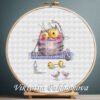 Cross stitch embroidery of a cute yoga cat sitting on a mat with small props and bright colors, displayed in a wooden hoop