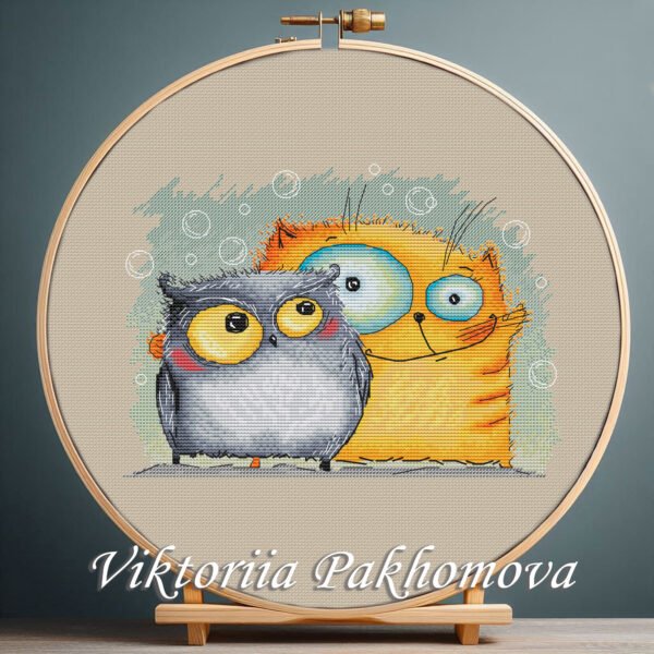 Cross stitch embroidery of a cheerful cat and owl standing together with bright colors and playful details, displayed in a wooden hoop