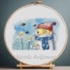 131 Cross stitch embroidery of a ginger cat with a hat surrounded by chamomile flowers and bees, displayed in a wooden hoop