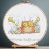 Cross stitch embroidery of a whimsical ginger cat with bright expressive eyes and playful decorative elements, displayed in a wooden hoop.