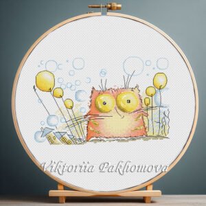 Cross stitch embroidery of a whimsical ginger cat with bright expressive eyes and playful decorative elements, displayed in a wooden hoop.