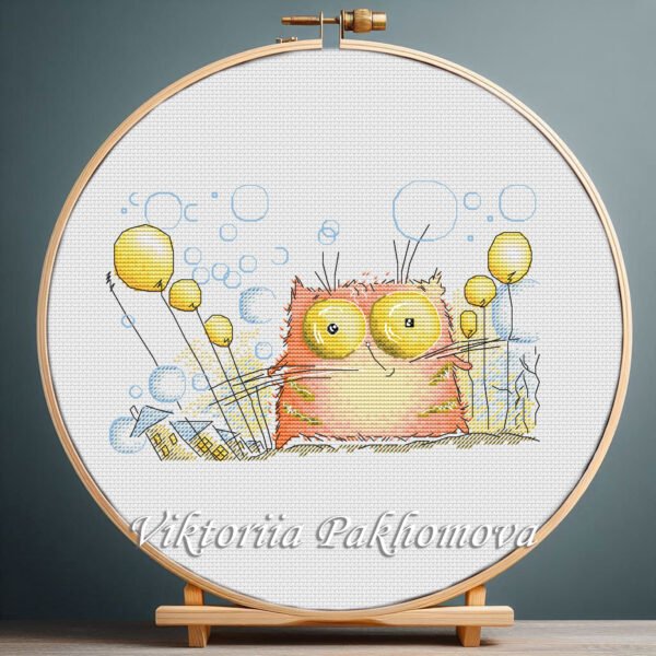 Cross stitch embroidery of a whimsical ginger cat with bright expressive eyes and playful decorative elements, displayed in a wooden hoop.