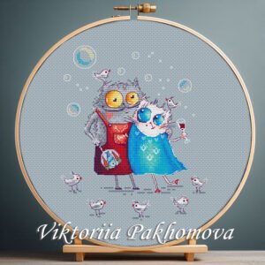 Cross stitch embroidery of two colorful whimsical cats with white birds and playful details, displayed in a wooden hoop