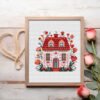 Framed cross stitch artwork of a floral folk art spring house with Scandinavian motifs and blooming flowers.