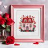Framed cross stitch artwork of a floral folk art spring house with Scandinavian motifs and blooming flowers.