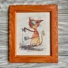 Framed cross stitch artwork featuring a whimsical ginger cat with a coffee cup and bold colorful shading.