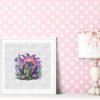 Framed cross stitch artwork of a purple fairy house surrounded by lavender flowers and summer greenery