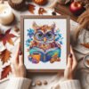 Framed owl cross stitch artwork with glasses, book, tea cup and golden acorns, vibrant autumn embroidery