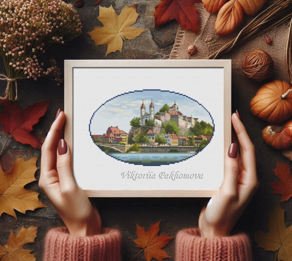 Framed Swiss castle cross stitch artwork with mountains and water, scenic European embroidery