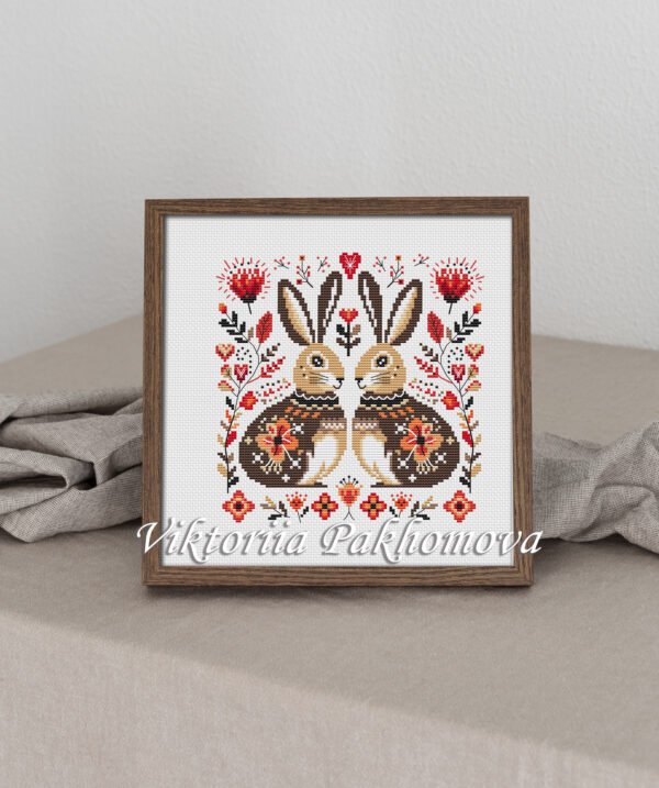 Framed cross stitch artwork of two romantic folk‑art bunnies surrounded by Scandinavian floral motifs