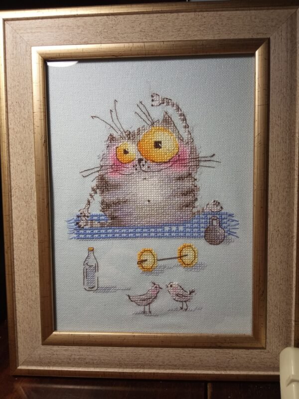 Framed cross stitch artwork of a funny kitten on a yoga mat with tiny props and colorful details