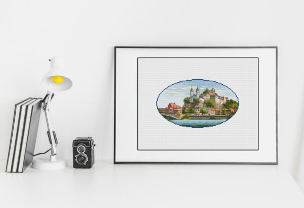 Framed Swiss castle cross stitch artwork with mountains and water, scenic European embroidery