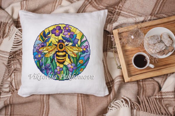 Stained glass bee cross stitch design displayed on decorative pillow