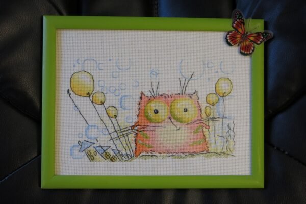 Framed cross stitch artwork featuring a cute whimsical ginger kitten with colorful details and a cheerful nursery style.