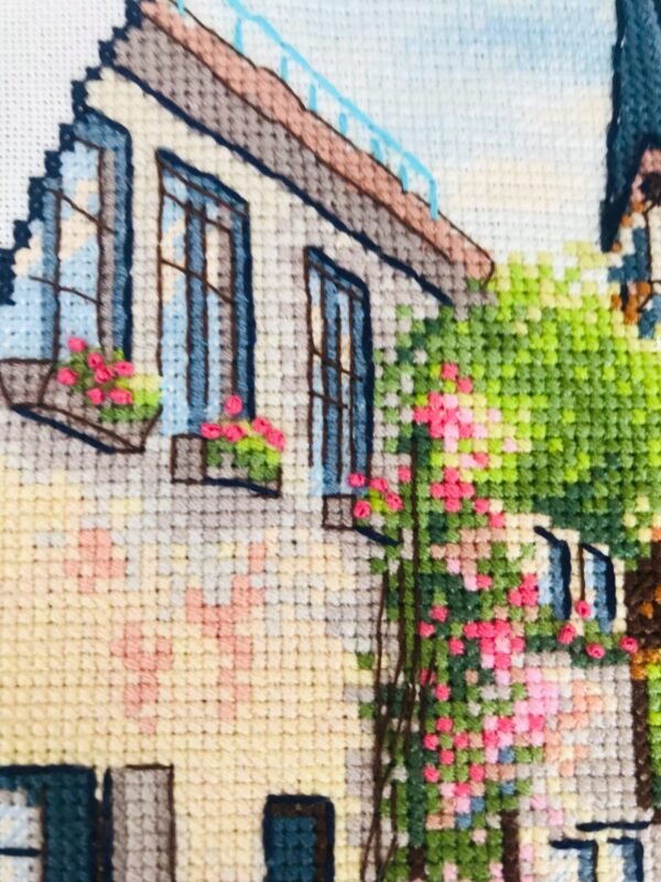 Close‑up of Neuruppin city cross stitch with buildings, flowers, and blue car