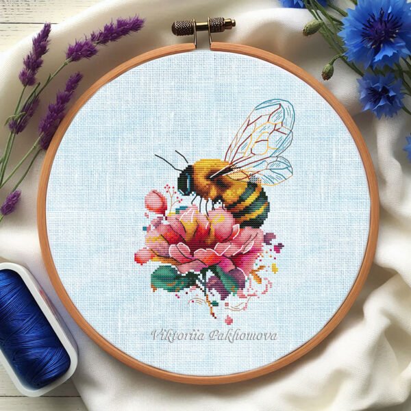 Peony and bee cross stitch pattern in a wooden embroidery hoop, detailed botanical floral design in pink and yellow tones