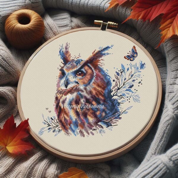 Mystical owl cross stitch in wooden hoop with autumn leaves and yarn, warm seasonal embroidery setup