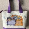 Cross stitch embroidery of a cheerful cat and owl standing together with bright colors and playful details, displayed on tote bag