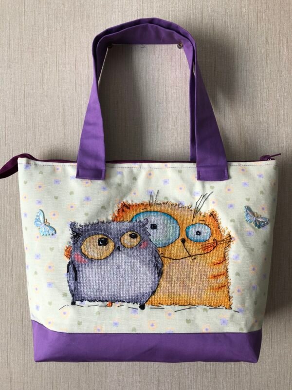 Cross stitch embroidery of a cheerful cat and owl standing together with bright colors and playful details, displayed on tote bag
