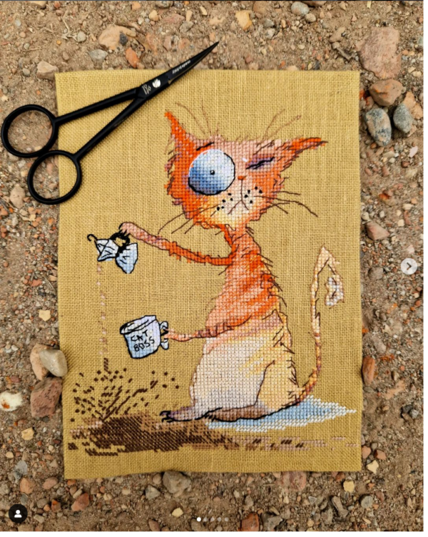 Finished embroidery of cross stitch artwork featuring a whimsical ginger cat with a coffee cup and bold colorful shading.