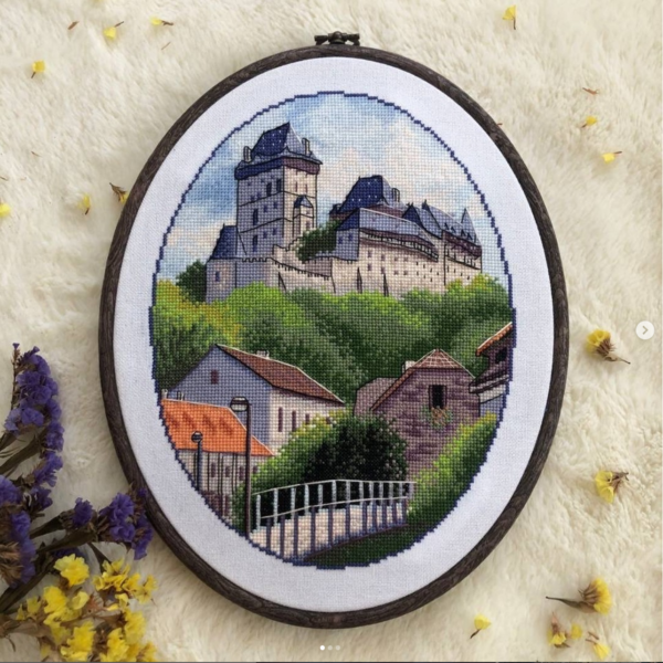 Framed Karlstein Castle cross stitch artwork with European village and castle towers