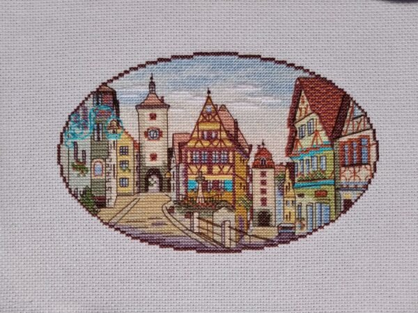Framed Rothenburg Germany cross stitch displayed with cozy decor, vibrant medieval town embroidery