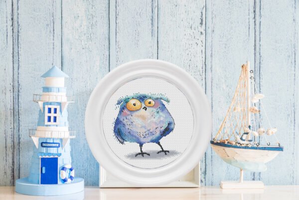 Framed cross stitch artwork of a whimsical tawny owl in soft watercolor‑ style colors