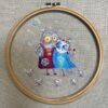 finished cross stitch artwork featuring two romantic cats with bright colors, tiny birds and soft decorative elements
