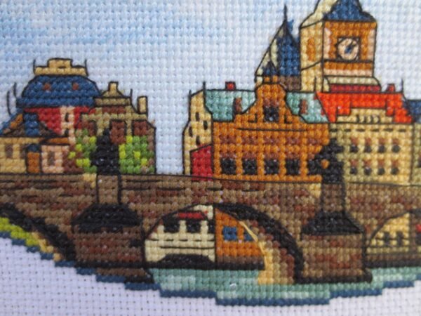 il_1588xN.2951291422_m5dg Prague Charles Bridge cross stitch displayed with cozy decor, vibrant European travel embroidery