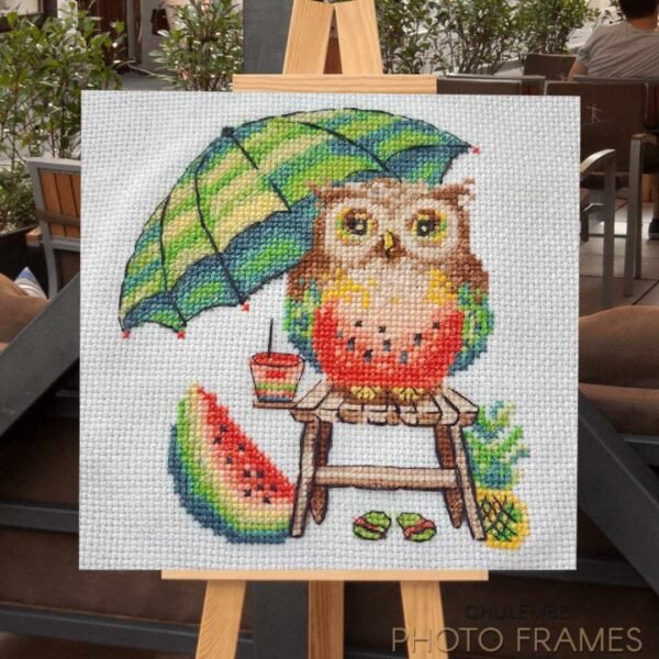 Watermelon owl cross stitch artwork on easel outdoors, colorful summer embroidery