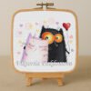 Cross stitch embroidery of two romantic cats with colorful hearts and playful details, displayed in a wooden hoop