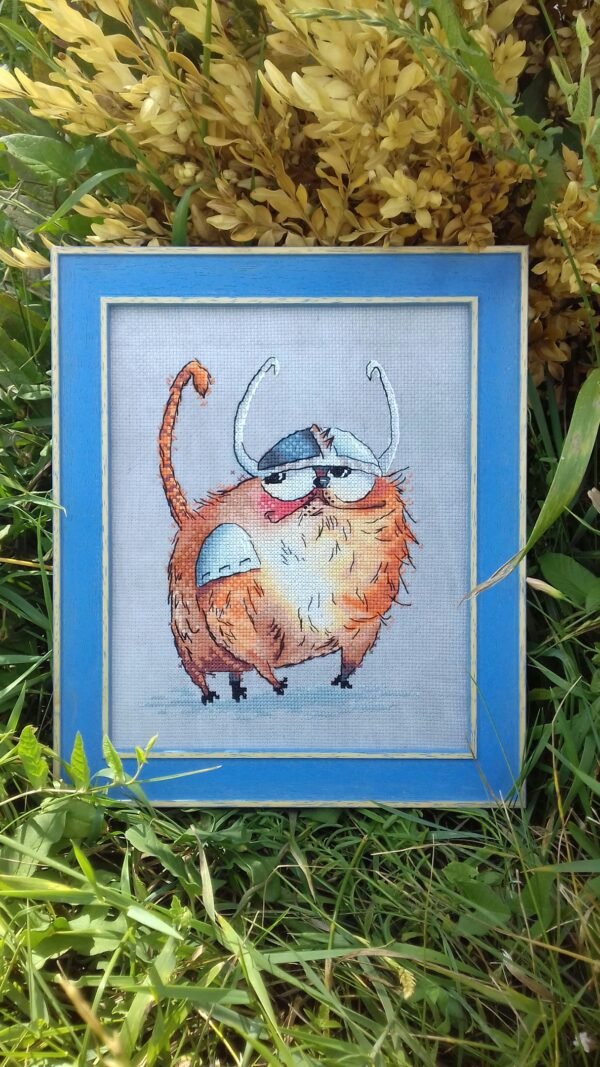framed cross stitch artwork of a Viking‑themed ginger cat with expressive details and warm colors.