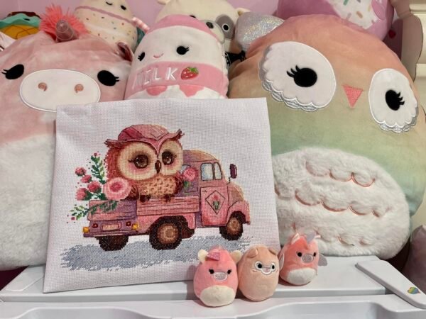 Baby owl and pink truck cross stitch artwork surrounded by plush toys, colorful children’s decor