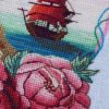 Coastal lighthouse cross stitch pattern displayed in a frame with floral peonies