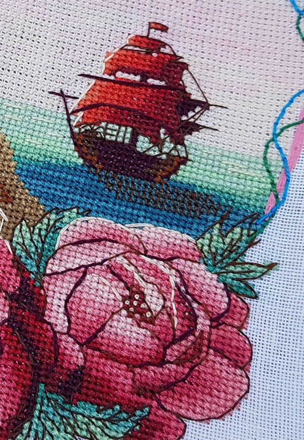 Coastal lighthouse cross stitch pattern displayed in a frame with floral peonies