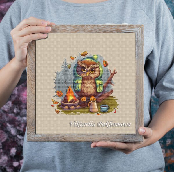 Framed cross stitch of a funny owl in a forest camping scene with warm autumn colors