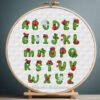 Cross stitch embroidery of a colorful ladybug alphabet with insect‑shaped letters displayed in a wooden hoop