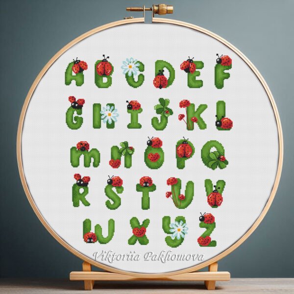 Cross stitch embroidery of a colorful ladybug alphabet with insect‑shaped letters displayed in a wooden hoop