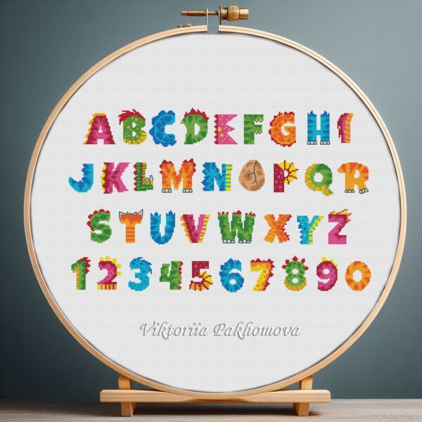 Cross stitch embroidery of a colorful dinosaur alphabet with rainbow Jurassic letters displayed in a wooden hoop