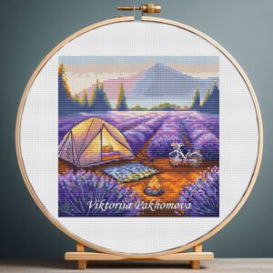 Cross stitch embroidery of a lavender camping scene with a tent, bicycle and mountains in a wooden hoop.