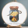 Cross stitch embroidery of a glass jar with a tent, campfire and forest landscape held in a wooden hoop
