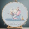Cross stitch embroidery of an elephant, a bunny and a cat sitting in a small paper boat with soft pastel details in a wooden hoop