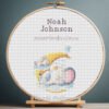 Cross stitch embroidery of a personalized bunny and elephant birth record displayed in a wooden hoop with custom newborn details.