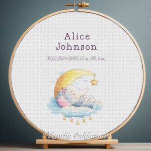 Cross stitch embroidery of a personalized baby elephant birth announcement displayed in a wooden hoop with custom newborn details