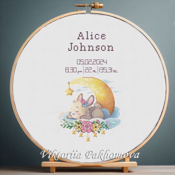 Cross stitch embroidery of a personalized sleeping bunny birth announcement displayed in a wooden hoop with custom newborn details