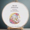 Cross stitch embroidery of a personalized sleeping bunny birth announcement displayed in a wooden hoop with custom newborn details.